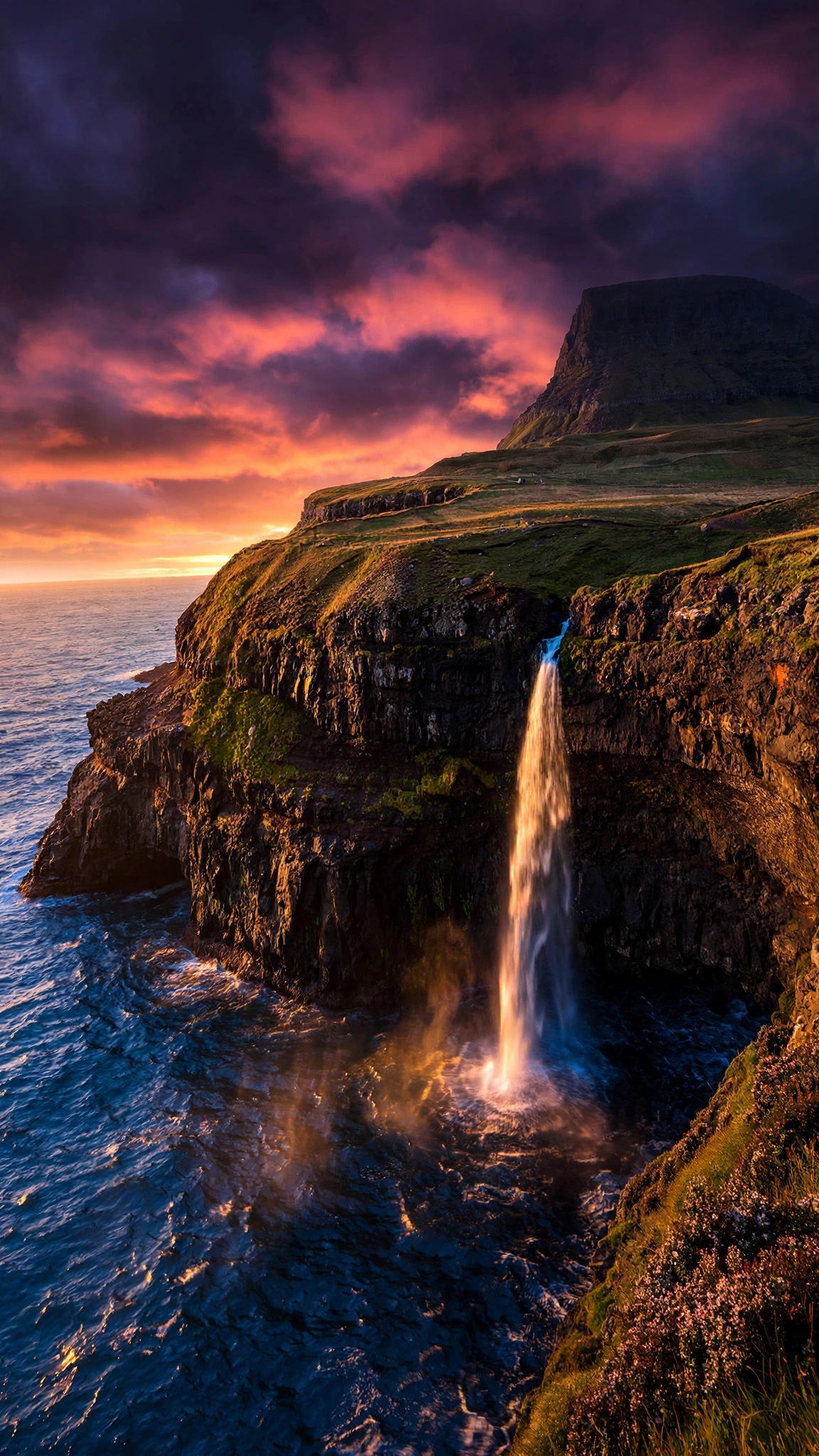 Mulafossur waterfall falling into the ocean at sunset in the Faroe Islands