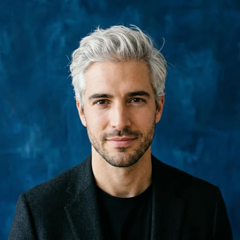 An adult man with silver hair and black blazer against indigo