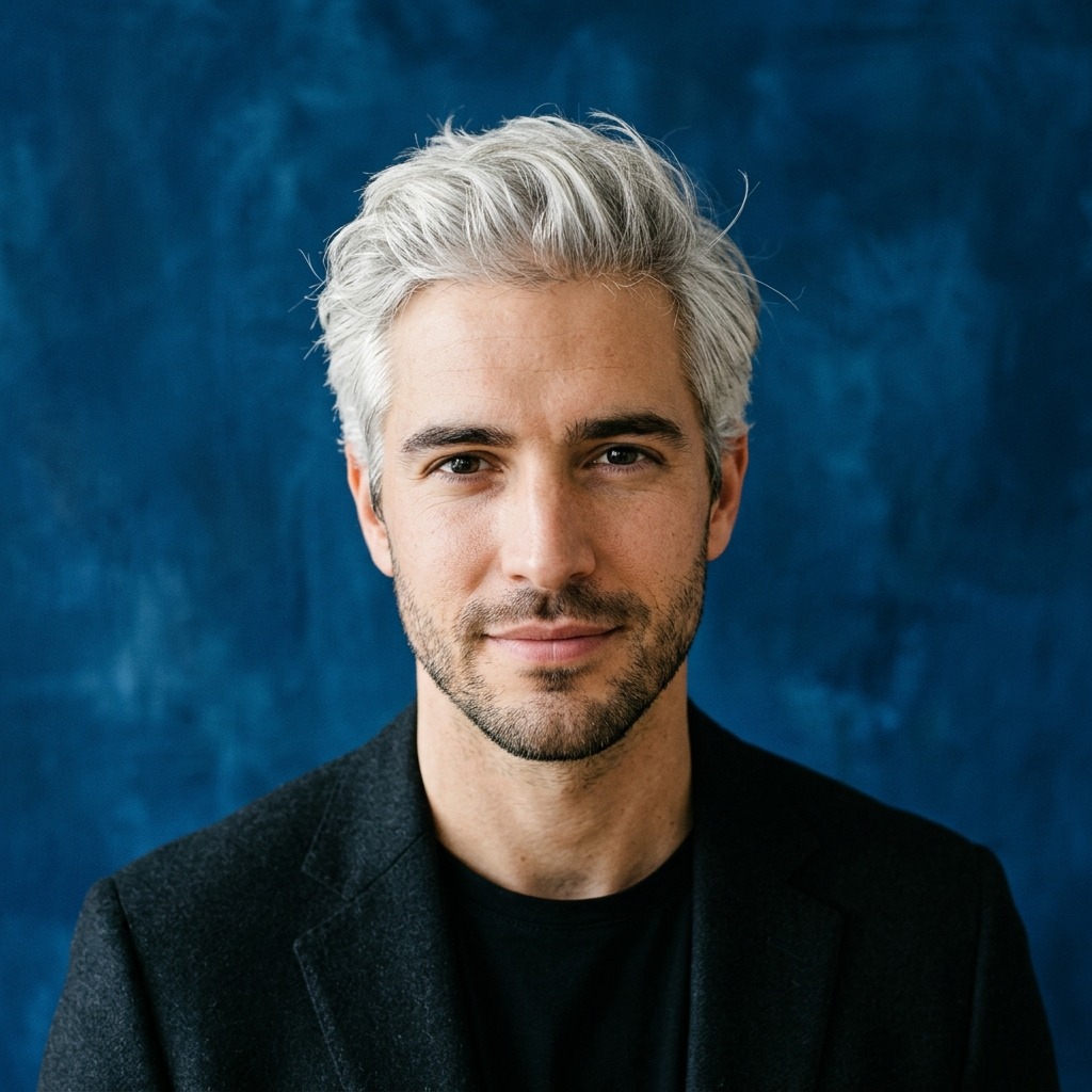 An adult man with silver hair and black blazer against indigo