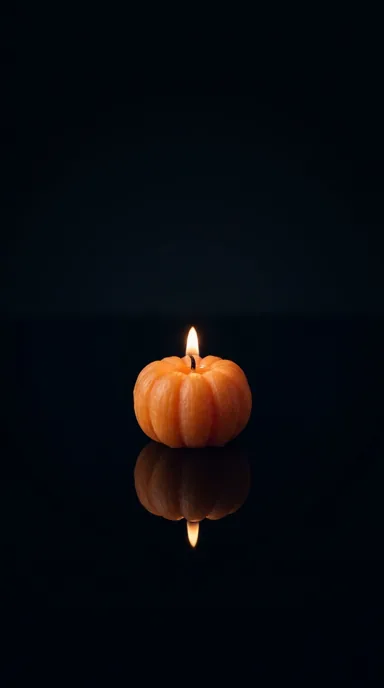 A small pumpkin candle and its reflection glow against a dark background