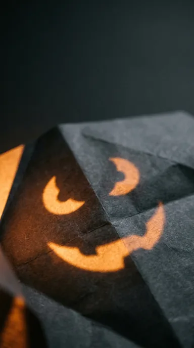 A carved pumpkin face appears as warm projected light on folded charcoal paper