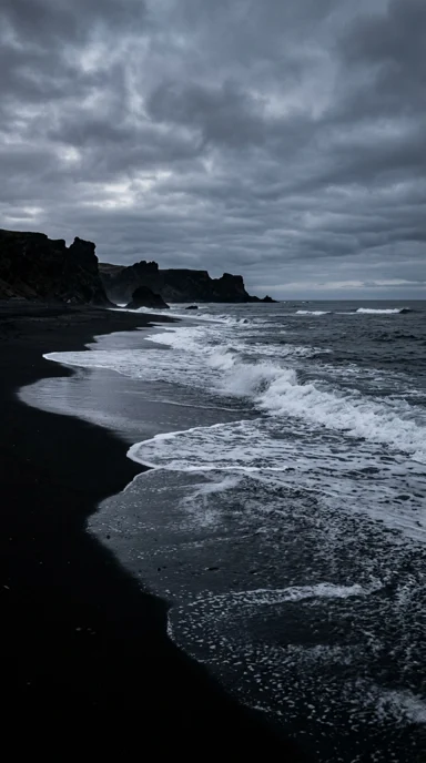 A black sand beach and pale surf.