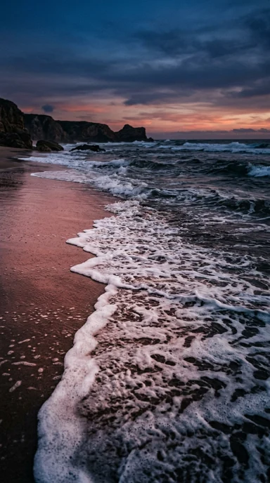 A foamy surf line on rose-colored sand.