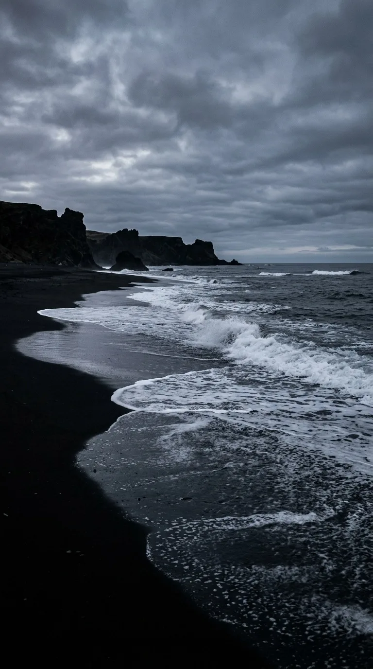 A black sand beach and pale surf.